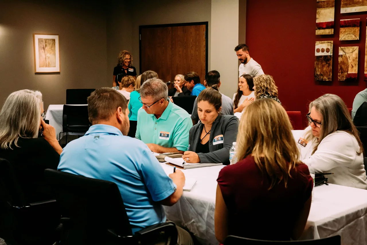 An EOS session part-way through: people at tables in small groups, notebooks and issues lists open in front of them, working a problem rather than watching a presentation.